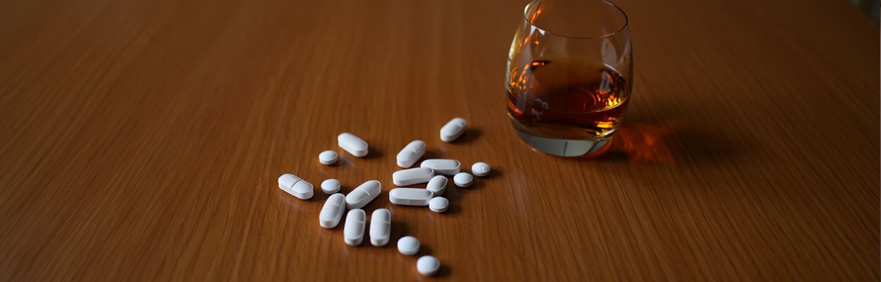 На столе лежат таблетки и рядом стоит стакан с алкоголем